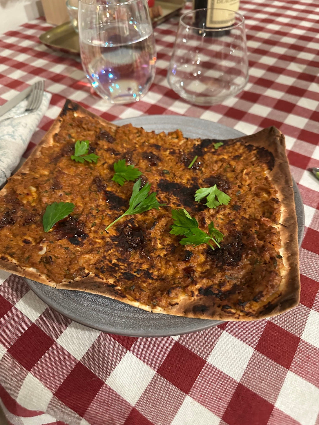 A freshly-baked flatbread with herbs, atop a checkered tablecloth.